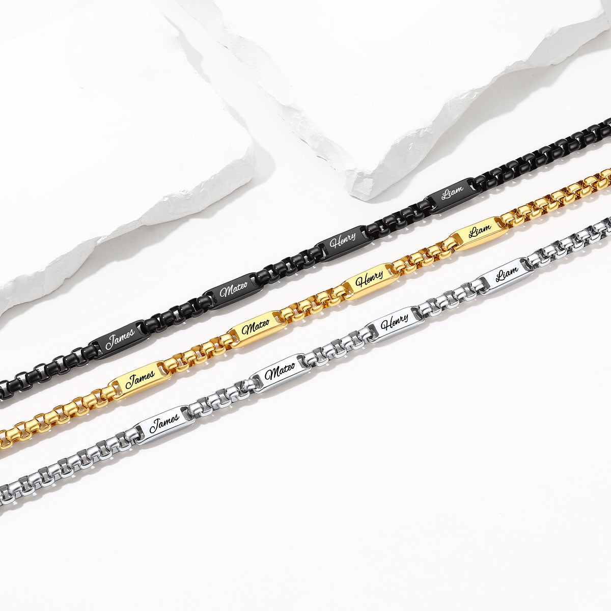 Three personalized name chains in black, gold, and silver, laid diagonally on a white background with decorative torn paper.