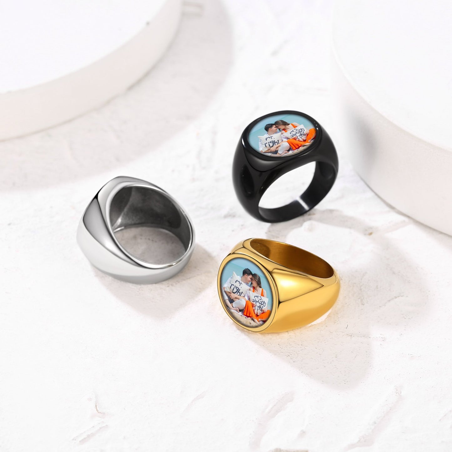 Three personalized picture signet rings in gold, silver, and black on a white fabric background.