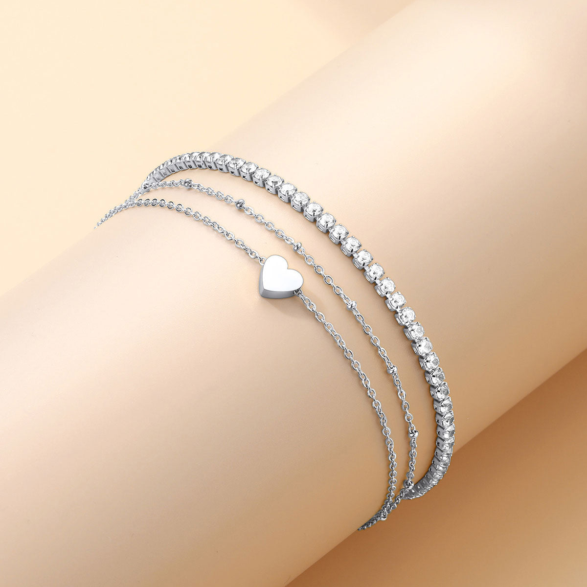 Three silver ankle bracelets set with a heart charm on a beige background