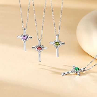 Three silver cross pendant necklaces with heart-shaped settings and colored gemstones (purple, red, and green) are displayed on a warm beige background, with a close-up of one necklace in the lower right corner.