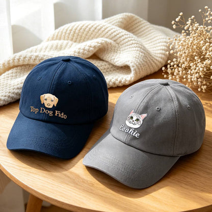 Two baseball caps displayed on a wooden table with a cream knit blanket and dried flowers in the background. The left cap is navy blue with an embroidered yellow dog face and the text 'Top Dog Fido'.