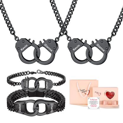 Two black handcuff-shaped necklaces and two matching black handcuff bracelets with engraved names, shown alongside a peach gift bag and a small gift box on a white background.