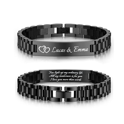 Two black metal link medical alert bracelets shown on a white background, one displaying the front with engraved text 'Lucas & Emma' and two heart shapes, and the other showing the inside with a sentimental quote.