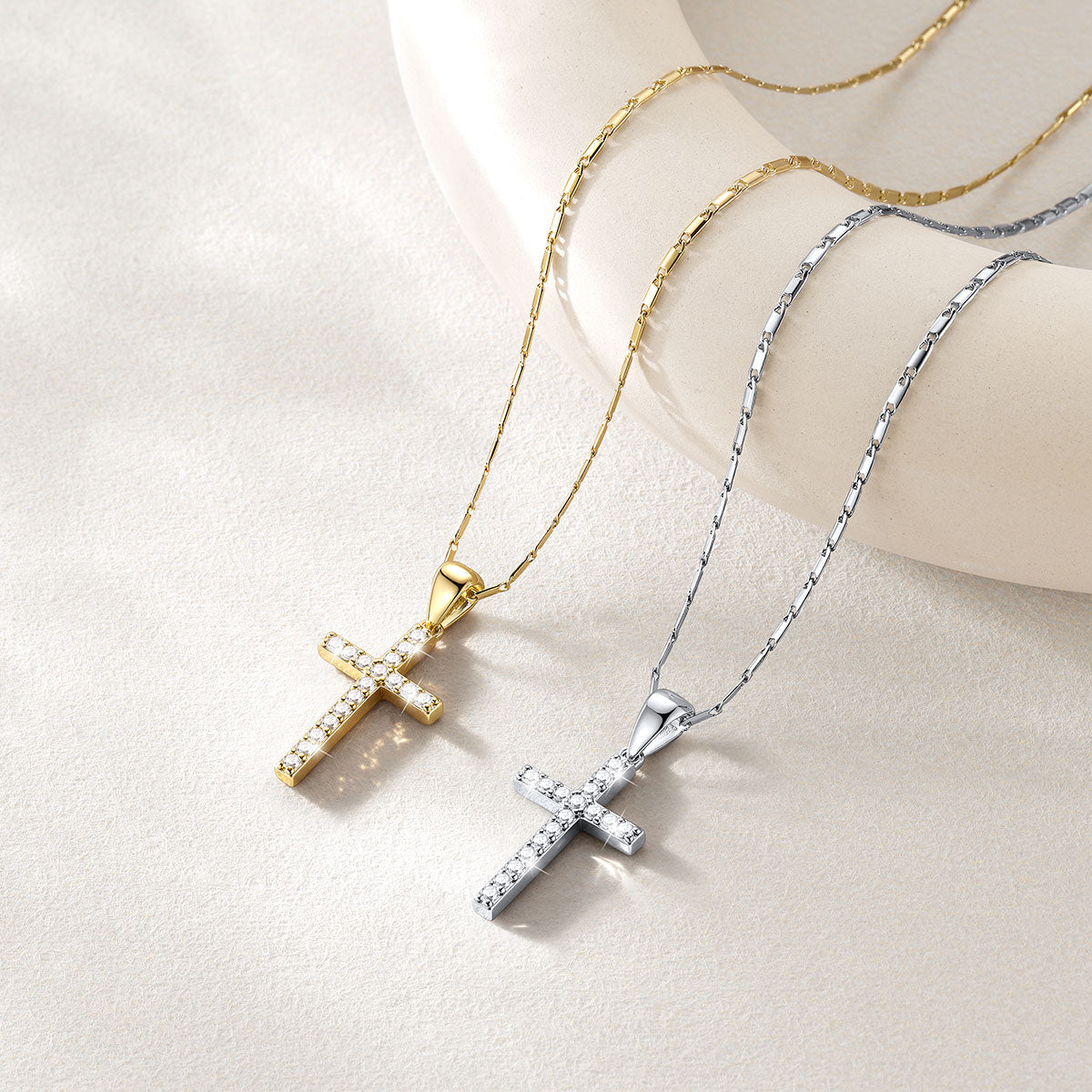 Two cross necklaces displayed on a cream-colored mannequin bust. One necklace is gold with a gold chain and a gold cross paved with small clear stones.