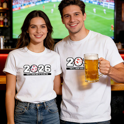 Two people wearing '2026' world cup t-shirts, one holding a beer mug, in front of a sports event on TV.