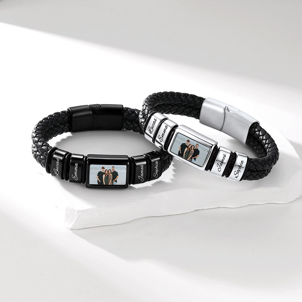 Two personalized black braided leather bracelets with rectangular metal charms, one in black and one in silver, each featuring a custom photo insert and engraved names, displayed on a white surface.