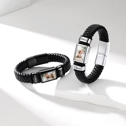 Two personalized braided black custom photo leather bracelet wristlets with silver-toned photo display panels and white nameplates, arranged on a clean white surface with soft shadows.