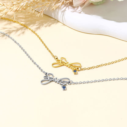 Two personalized name necklaces with script lettering pendants, one in gold and one in silver, both with small blue stone accents, displayed on a light cream background with dried floral elements.