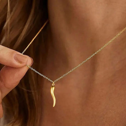 Gold necklace with a unique pendant held by a hand against a blurred background