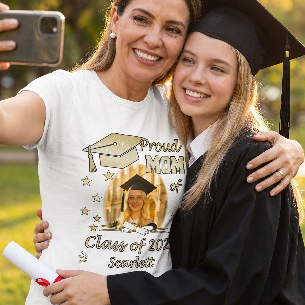 Woman wearing a 'Proud Mom of Class of 2026' graduation t shirt taking a selfie with a graduate.