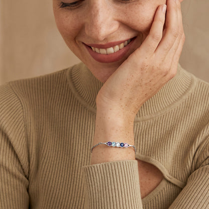 Woman wearing a pea in pot birthstone bracelet with colorful beads, smiling and touching her face.