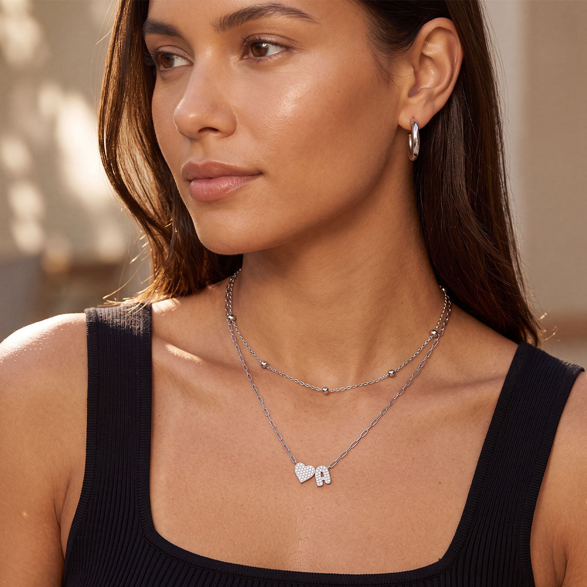 Woman wearing a silver initial necklace with heart-shaped pendants.