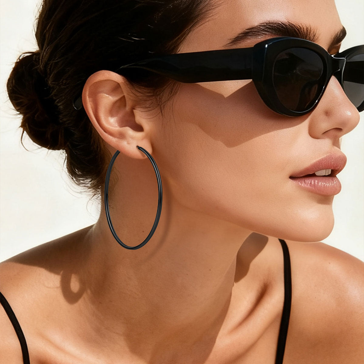 Woman wearing black hoop earrings and sunglasses with a neutral background