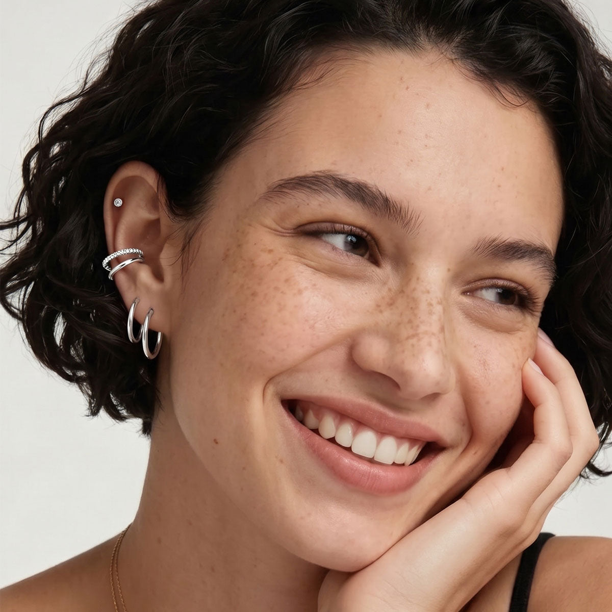 Woman wearing silver huggie earrings with a neutral background